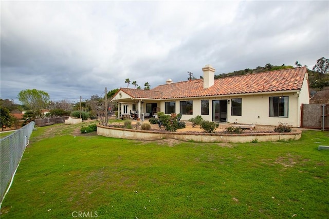 rear view of house featuring a tile roof, a chimney, a lawn, and a fenced backyard