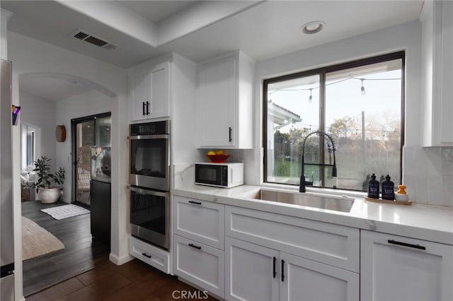 kitchen with double oven, white cabinets, a sink, and visible vents