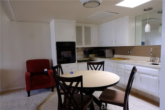 kitchen with a sink, white cabinetry, black oven, light countertops, and decorative backsplash