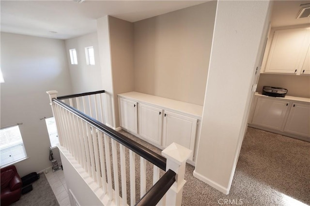 hallway with baseboards, visible vents, and an upstairs landing