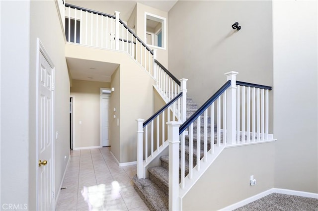 stairway with a high ceiling, tile patterned flooring, and baseboards