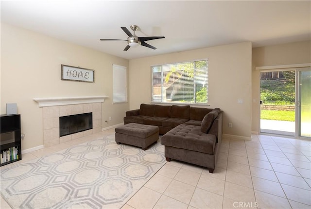 living room with light tile patterned floors, a tiled fireplace, a ceiling fan, and baseboards