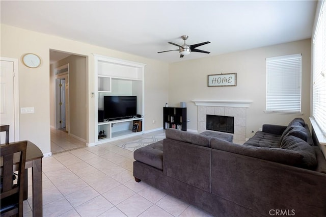 living room featuring built in features, light tile patterned floors, a ceiling fan, a tile fireplace, and baseboards