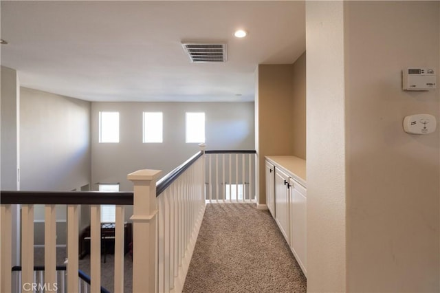 hallway with carpet floors, visible vents, and an upstairs landing