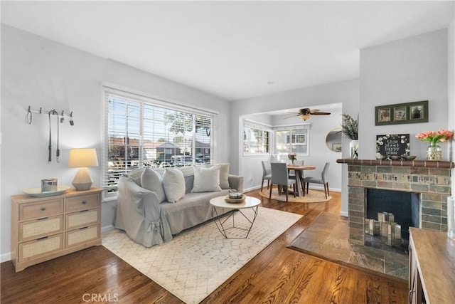 living room featuring a fireplace, wood finished floors, baseboards, and a ceiling fan