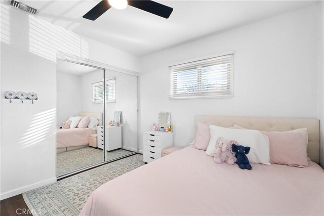 bedroom with visible vents, wood finished floors, a closet, baseboards, and ceiling fan