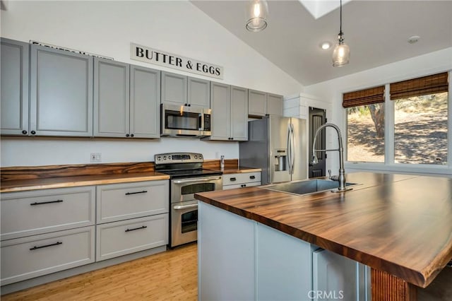 kitchen featuring lofted ceiling, butcher block counters, appliances with stainless steel finishes, light wood-style floors, and a sink