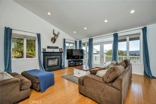 living area with vaulted ceiling, plenty of natural light, a fireplace with flush hearth, and light wood-style floors