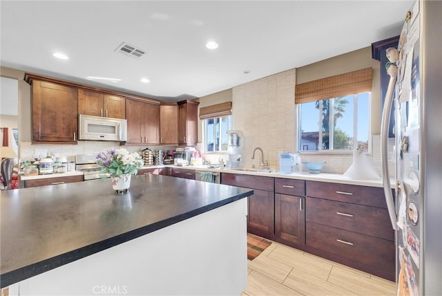 kitchen with visible vents, decorative backsplash, white microwave, freestanding refrigerator, and a sink