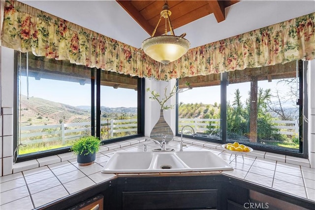 kitchen with lofted ceiling with beams, tile countertops, dark cabinetry, and a sink