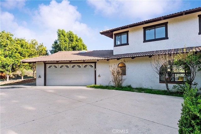 mediterranean / spanish home with a garage, concrete driveway, a tiled roof, and stucco siding