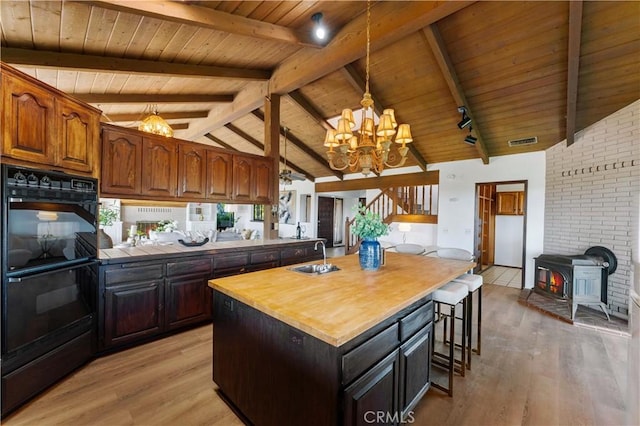 kitchen with dobule oven black, light wood-style flooring, wood counters, vaulted ceiling with beams, and a sink