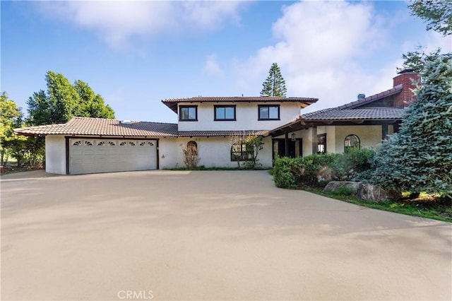 mediterranean / spanish house with a garage, stucco siding, driveway, and a tiled roof