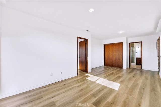 unfurnished bedroom featuring light wood-style floors, connected bathroom, baseboards, and a closet