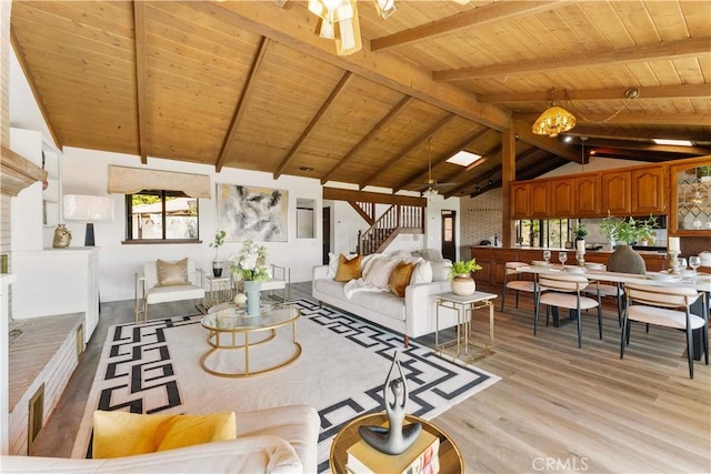 living area with lofted ceiling with beams, a ceiling fan, wood ceiling, light wood-type flooring, and stairs