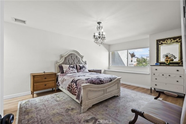 bedroom with visible vents, a notable chandelier, baseboards, and wood finished floors