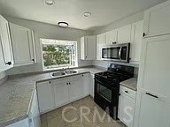 kitchen featuring stainless steel microwave, black range with gas stovetop, a sink, and white cabinetry