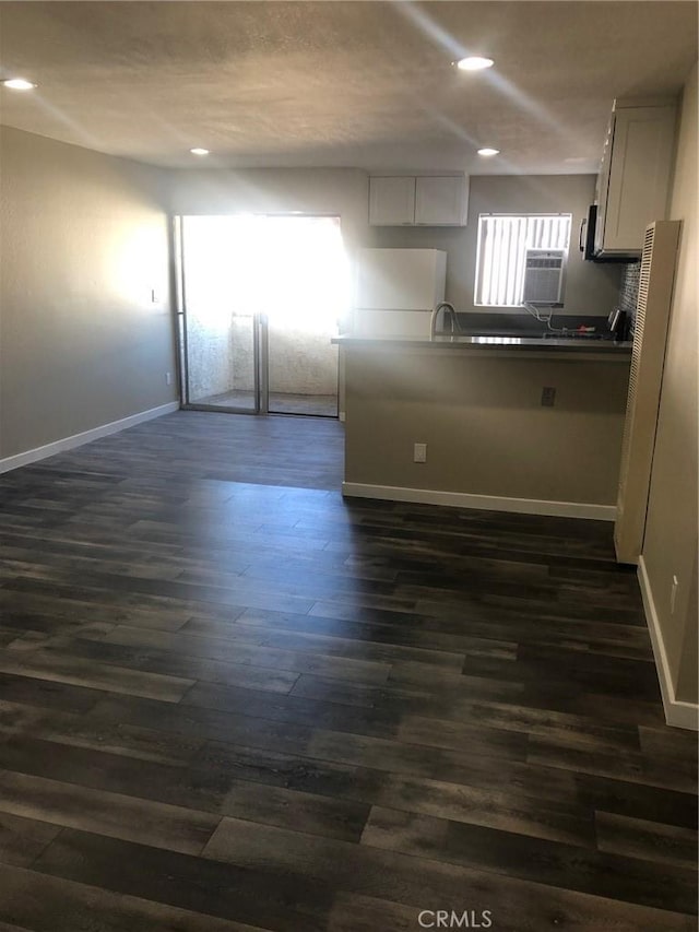 kitchen with dark wood-type flooring, fridge, dark countertops, and baseboards