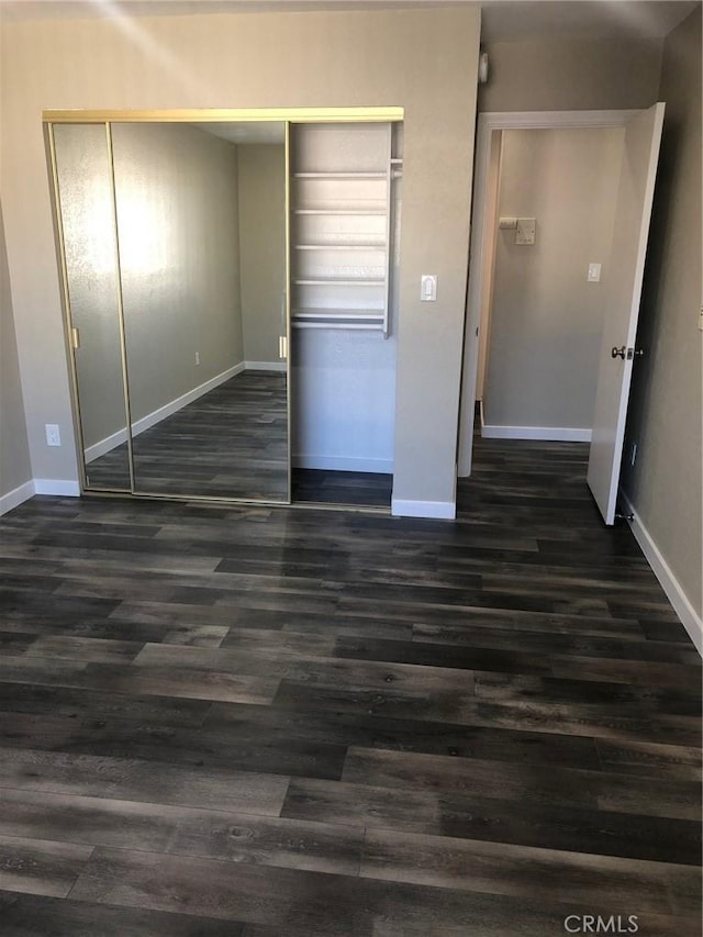 unfurnished bedroom with a closet, baseboards, and dark wood-type flooring