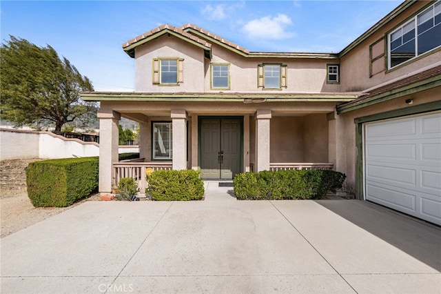 view of front of house featuring a porch, a tiled roof, a garage, and stucco siding