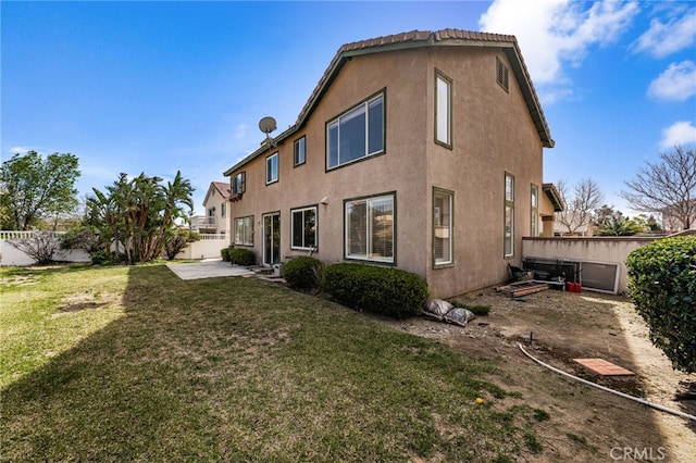 rear view of house featuring a patio area, a yard, fence, and stucco siding