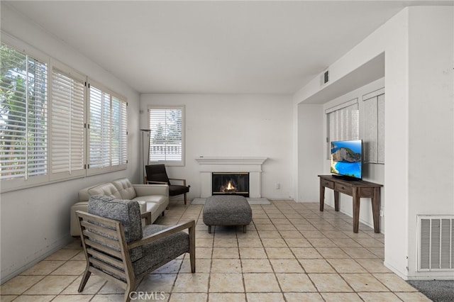 living area with a glass covered fireplace, visible vents, and light tile patterned floors