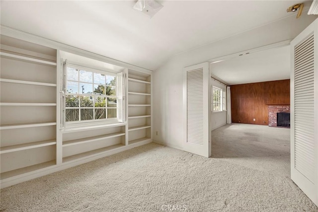 carpeted spare room with wood walls, a brick fireplace, and built in shelves