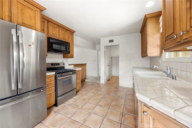 kitchen featuring light tile patterned floors, tile countertops, appliances with stainless steel finishes, a sink, and backsplash