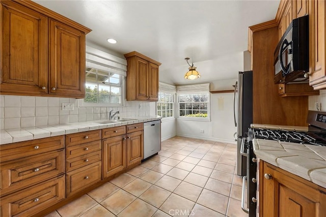 kitchen with tasteful backsplash, appliances with stainless steel finishes, brown cabinets, a sink, and light tile patterned flooring