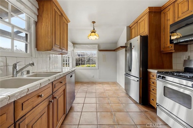 kitchen with brown cabinetry, backsplash, stainless steel appliances, a sink, and light tile patterned flooring