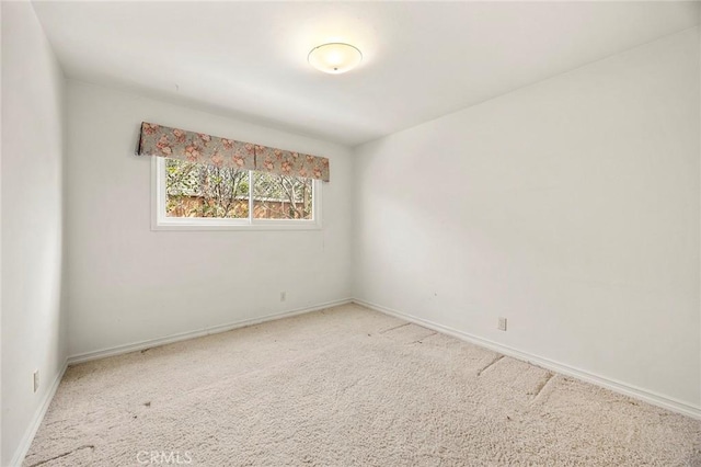 spare room with baseboards and light colored carpet