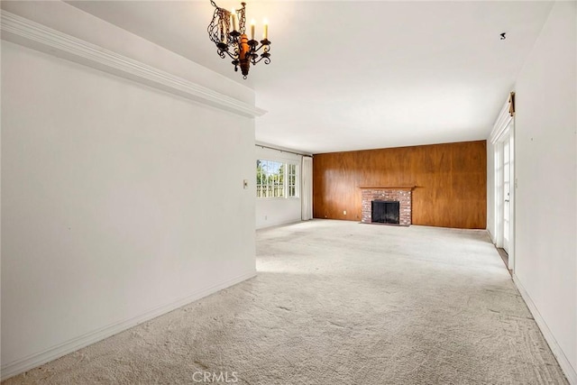 unfurnished living room featuring light carpet, wooden walls, baseboards, a brick fireplace, and a chandelier