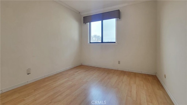 spare room featuring light wood finished floors, baseboards, and crown molding