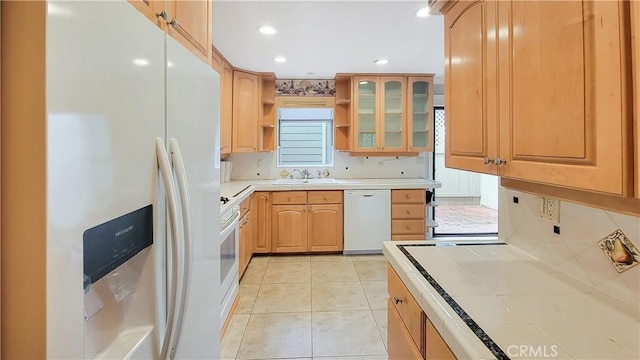 kitchen with light tile patterned flooring, white appliances, a sink, tile counters, and tasteful backsplash