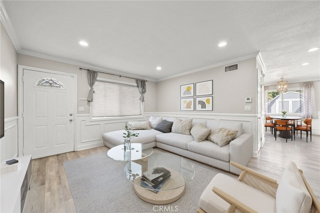 living room with light wood-type flooring, wainscoting, visible vents, and ornamental molding