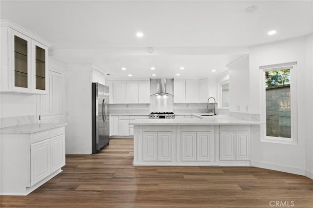 kitchen with a peninsula, a sink, light countertops, wall chimney range hood, and freestanding refrigerator