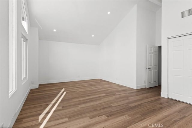 unfurnished bedroom with high vaulted ceiling, wood finished floors, visible vents, and baseboards