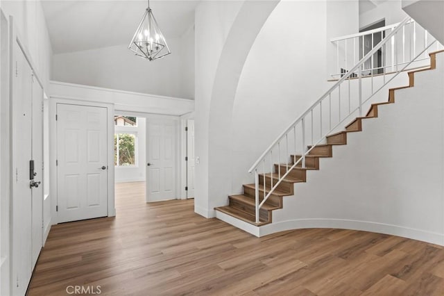 foyer entrance featuring arched walkways, high vaulted ceiling, stairway, and wood finished floors