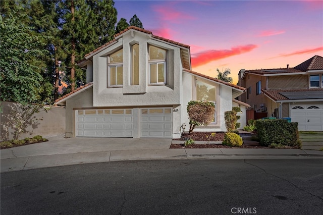 view of front facade with a garage, a tile roof, concrete driveway, and stucco siding