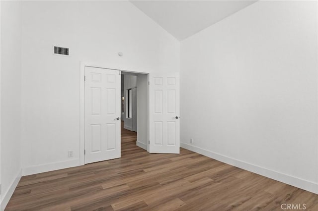 unfurnished bedroom with high vaulted ceiling, visible vents, baseboards, and wood finished floors