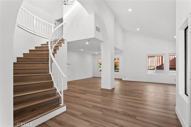 entrance foyer featuring visible vents, stairway, wood finished floors, high vaulted ceiling, and baseboards