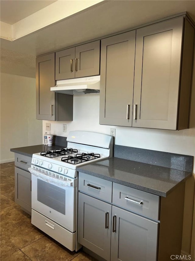 kitchen with under cabinet range hood, dark stone counters, white range with gas stovetop, and gray cabinetry