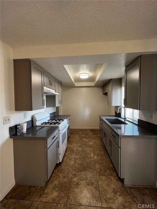 kitchen with white gas stove, a sink, under cabinet range hood, dark countertops, and a raised ceiling