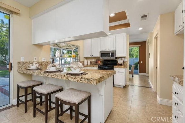 kitchen with a breakfast bar area, stainless steel microwave, visible vents, gas stove, and white cabinetry