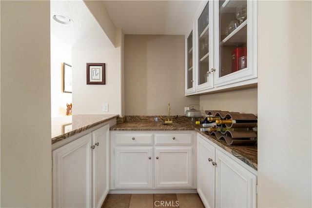 kitchen featuring dark stone counters, light tile patterned floors, glass insert cabinets, and white cabinets