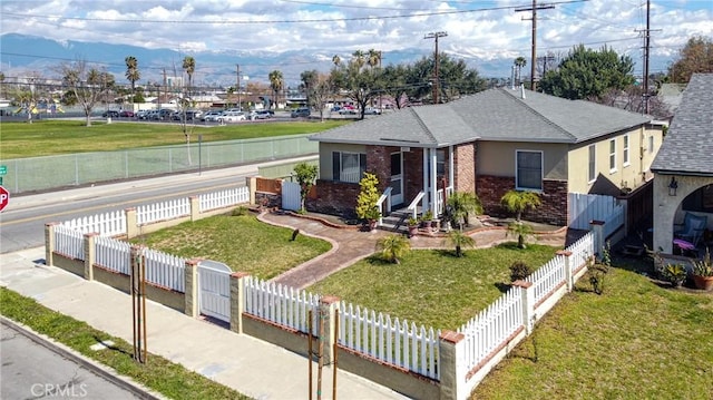 view of front of home featuring a fenced front yard, brick siding, a front lawn, and roof with shingles