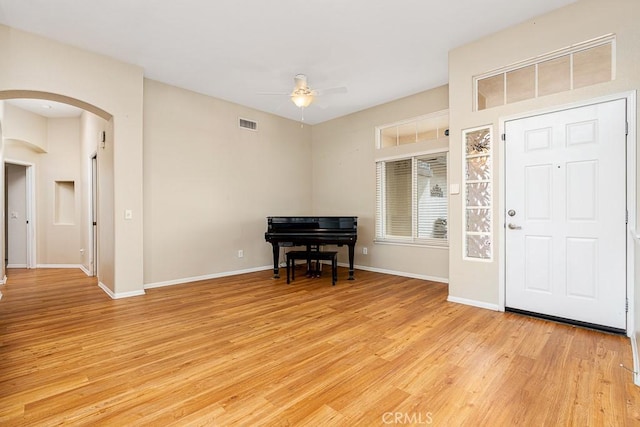 entryway featuring arched walkways, visible vents, a ceiling fan, baseboards, and light wood finished floors