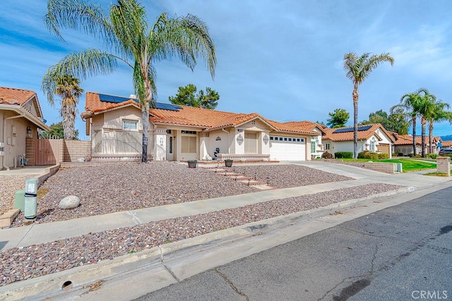 mediterranean / spanish-style house with a garage, a tile roof, concrete driveway, a gate, and roof mounted solar panels