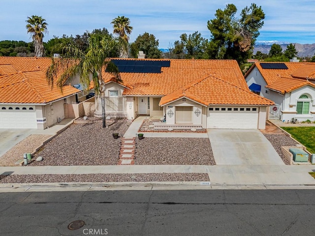 mediterranean / spanish house with a garage, a tiled roof, concrete driveway, roof mounted solar panels, and stucco siding