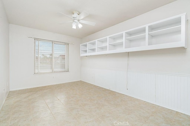 unfurnished room featuring a ceiling fan and a wainscoted wall